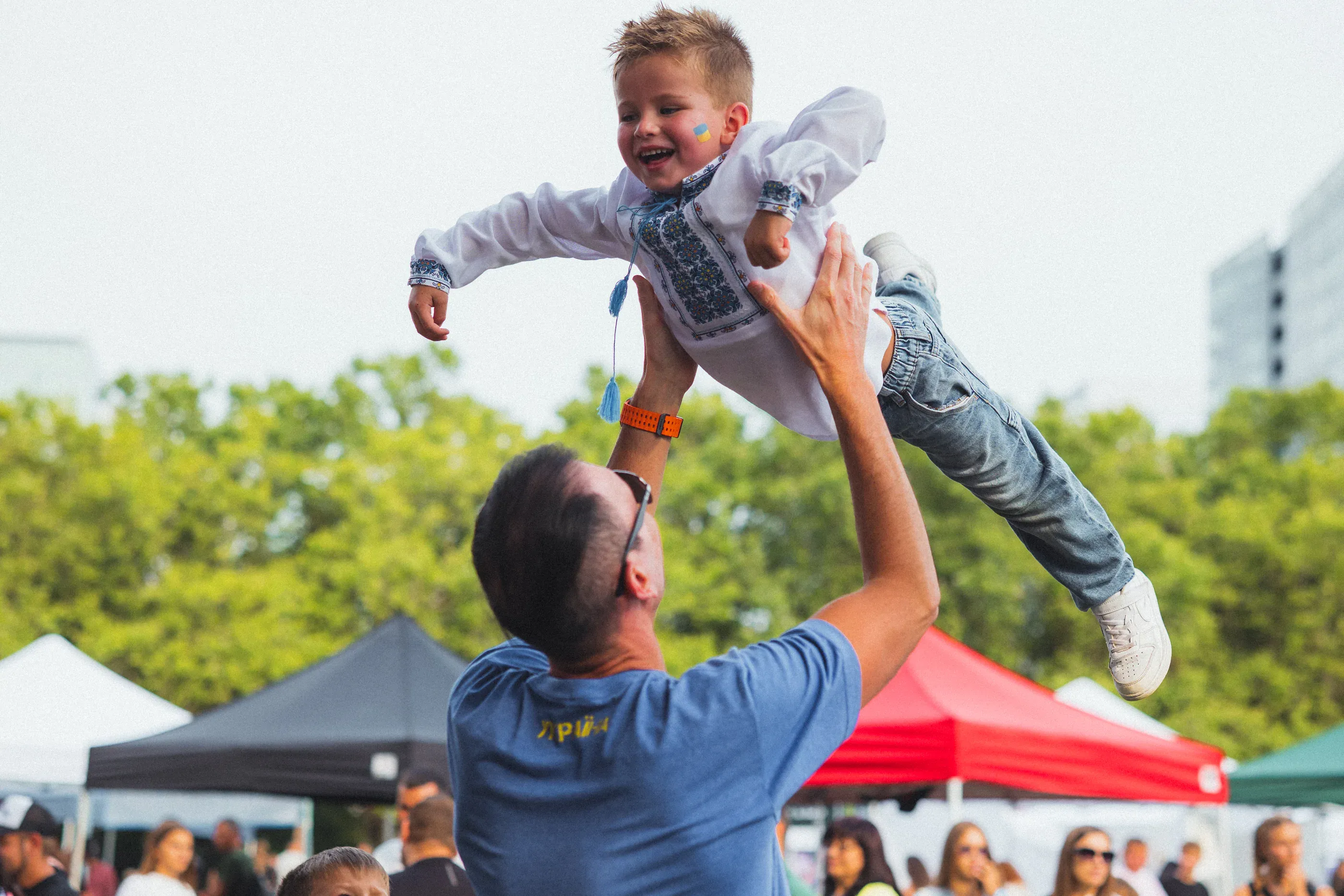 Adult lifts a child above an outdoor festival crowd.